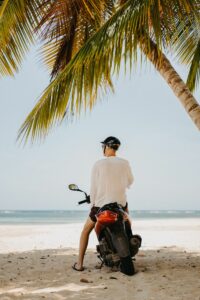 Man sitting on a scooter under palm trees on a sandy beach in the Dominican Republic.